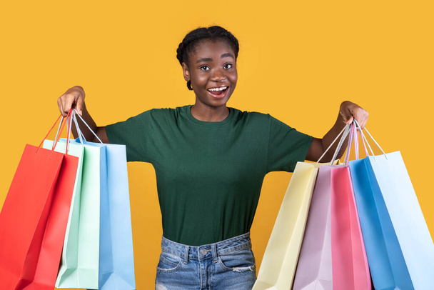 Joyeuse acheteuse sur le shopping posant avec des sacs, fond jaune - Photo, image