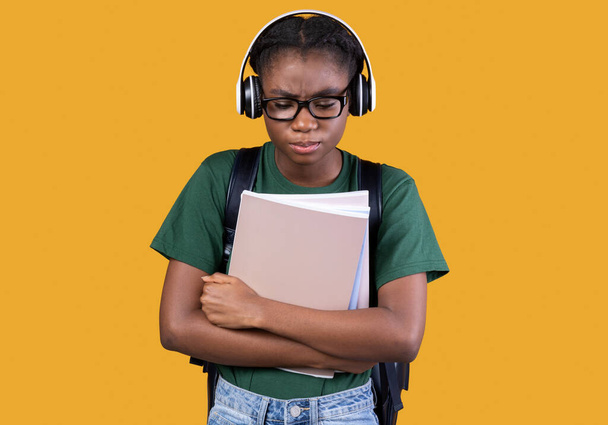Ongelukkig slachtoffer Afrikaanse meisje met Copybooks Staande over gele achtergrond - Foto, afbeelding