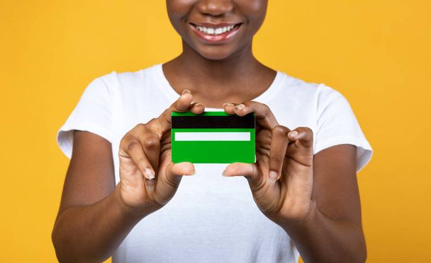 Mujer africana feliz mostrando tarjeta de crédito sobre fondo amarillo, recortado - Foto, imagen