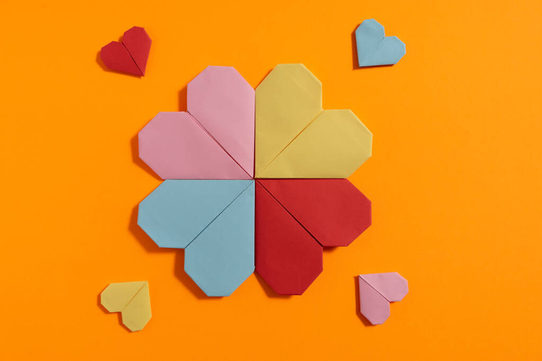 Καρδιές Origami φτιαγμένες με χρωματιστό χαρτί για συγχαρητήρια για την ημέρα του Αγίου Βαλεντίνου για τα ερωτευμένα ζευγάρια, σε πορτοκαλί φόντο. Έννοια αγάπης - Φωτογραφία, εικόνα
