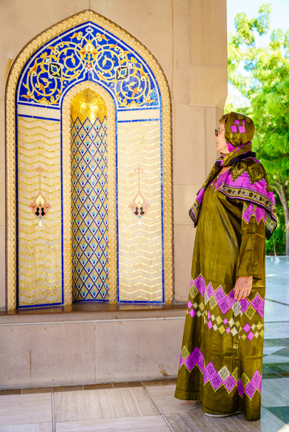 Una mujer vestida con un omani abaya tradicional mirando una alcoba ornamentada en la Gran Mezquita del Sultán Qaboos en Mascate, Omán - Foto, imagen
