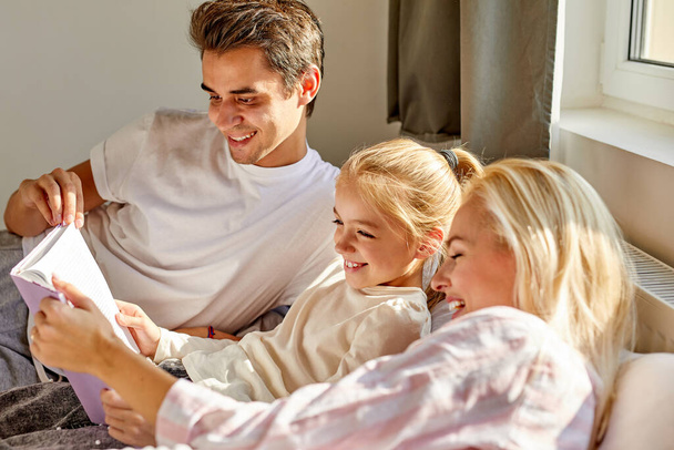 portrait of happy family reading a book together on bed - Фото, изображение
