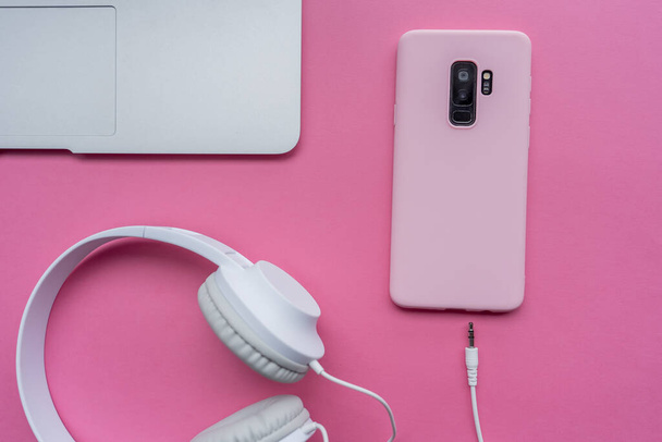 A high angle shot of a laptop, a cellphone, and headphones on a pink surface - Fotoğraf, Görsel