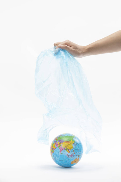 Függőleges felvétel egy kézről, amely eltávolítja a műanyag zsákot a földgömbről - környezetvédelmi koncepció - Fotó, kép