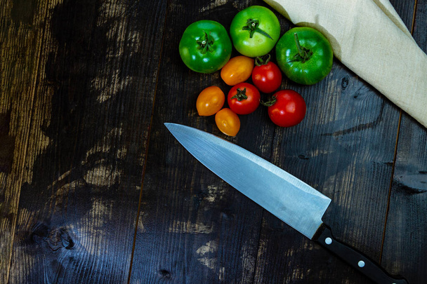 A top view of ripe and unripe tomatoes with a knife on a wooden table - Φωτογραφία, εικόνα