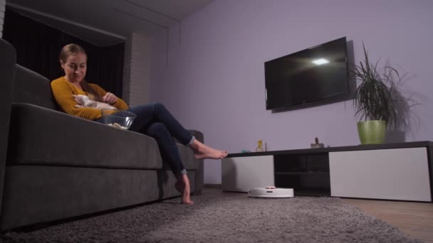 Staubsaugerroboter arbeitet, während sich Frau auf Sofa entspannt - Filmmaterial, Video