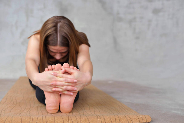Close up on feet of naked girl practicing paschimottanasana yoga asana. Woman on forward bend pose holding hands. Flexibility concep - Photo, Image