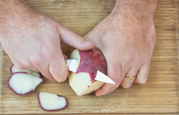 Man peeling a red potato with a small knife on a cutting board - Photo, Image