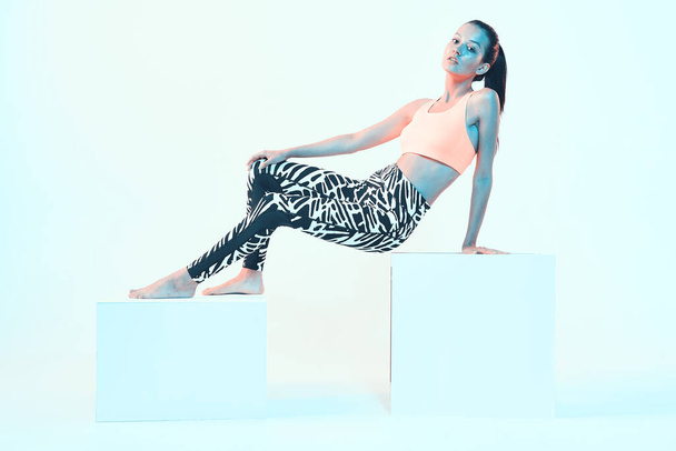 Sporty fit girl young in stylish sportswear posing in neon light in studio on cubes. Healthy sport lifestyle - Photo, Image