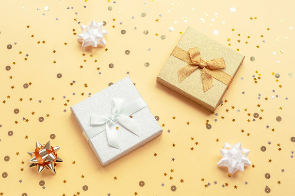 Two gifts in boxes on yellow backgound with baubles and confetti. Christmas, New Year concept. Top view, flat lay. - Photo, Image