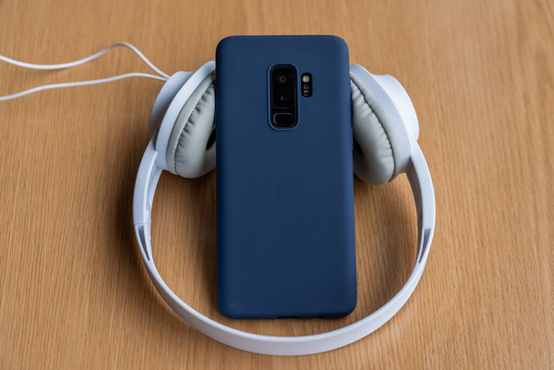 A high angle shot of a blue cellphone with headphones on a wooden surface - Фото, изображение