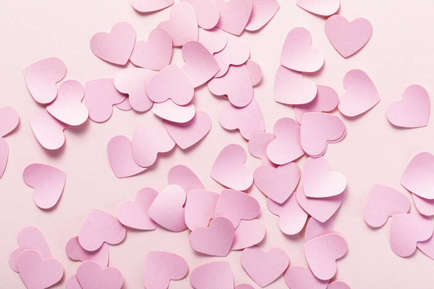 A top view shot of a heap of cute pink papers in a heart shape on a pink background - 写真・画像