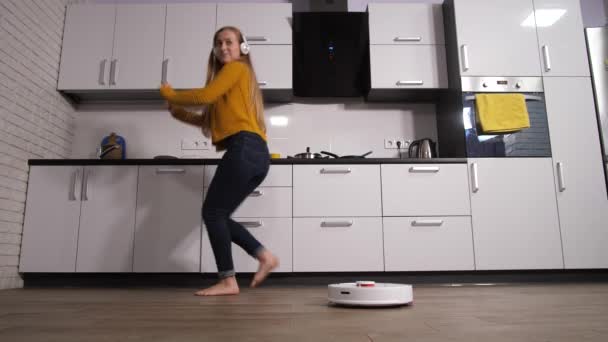Mujer bailando en la cocina mientras robot de limpieza - Metraje, vídeo