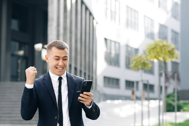 Successful businessman celebrating win with mobile phone outside. Surprised man looking mobile phone outside. Portrait of excited man reading good news at smartphone outdoors. - Foto, Imagem