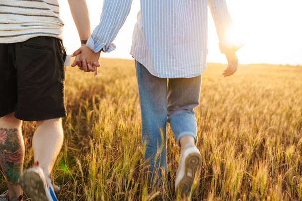 Photo recadrée d'un couple amoureux marchant ensemble à l'extérieur sur le terrain se tenant la main l'un de l'autre - Photo, image