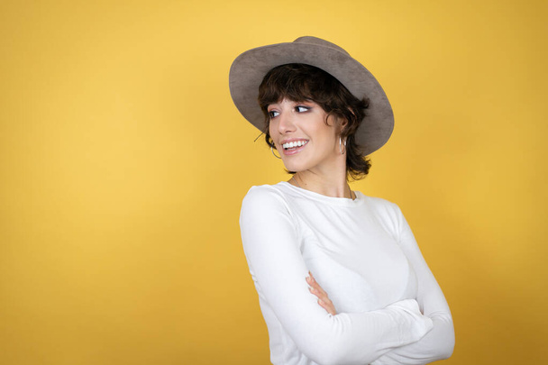 Young caucasian woman wearing hat over isolated yellow background smiling in profile looking back - Fotografie, Obrázek