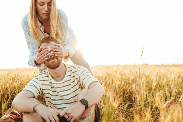 Image of happy woman covering eyes of her boyfriend sitting outside at the field - Photo, Image
