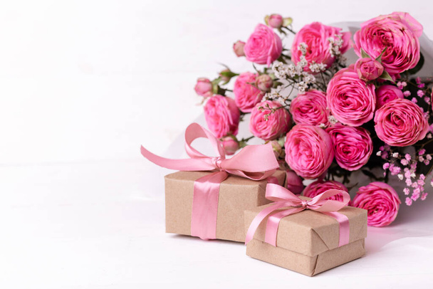 Szent Valentin-napi koncepció. Friss pasztell puha rózsaszín rózsák, és ajándékdobozok kraft papucsba csomagolva, szalagokkal fehér fa asztalon. - Fotó, kép