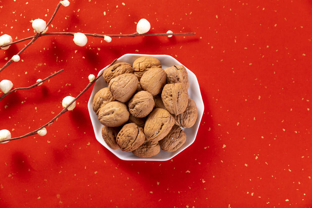 A top view shot of a bowl of walnuts on a beautiful red Christmas background decorated with willow twigs - Photo, image