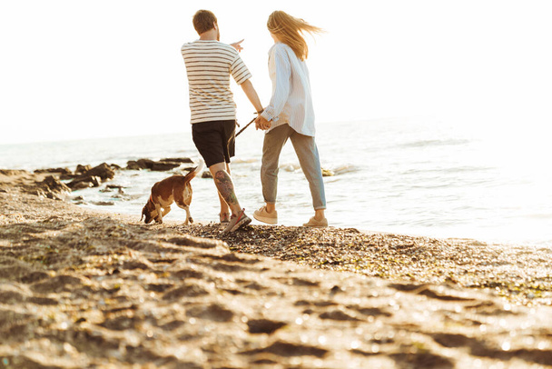 Photo of a young amazing loving couple with dog outside at the beach - 写真・画像