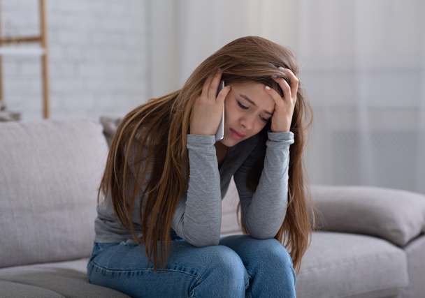Mujer joven disgustada hablando con su psicólogo en el teléfono celular, recibiendo ayuda en el tratamiento de la depresión en el hogar - Foto, imagen