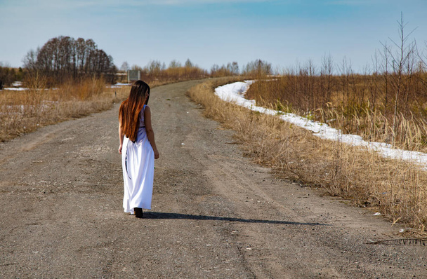 Brunette fille dans une robe blanche marchant sur une route - Photo, image
