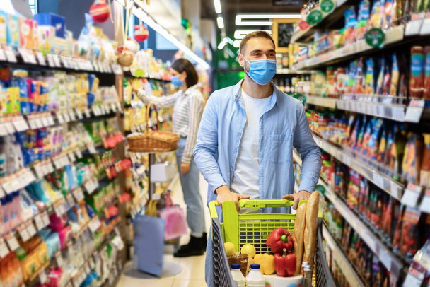 Молодой человек в маске с корзиной покупок в супермаркете - Фото, изображение