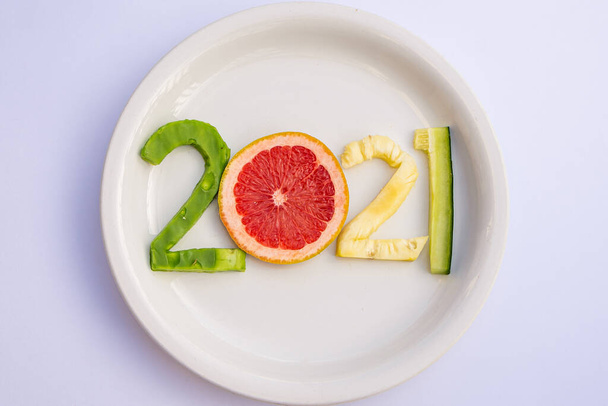 Deliciosas frutas cortadas en forma de año nuevo 2021 en un plato blanco sobre una mesa blanca. - Foto, imagen