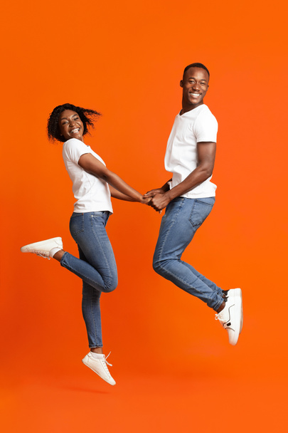 Emotional black couple in love holding hands and jumping up - Foto, Imagem