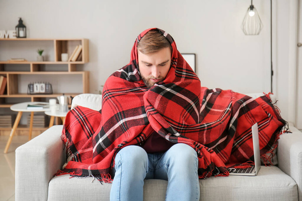 Freezing young man wrapped in warm plaid at home. Concept of heating season - Foto, afbeelding