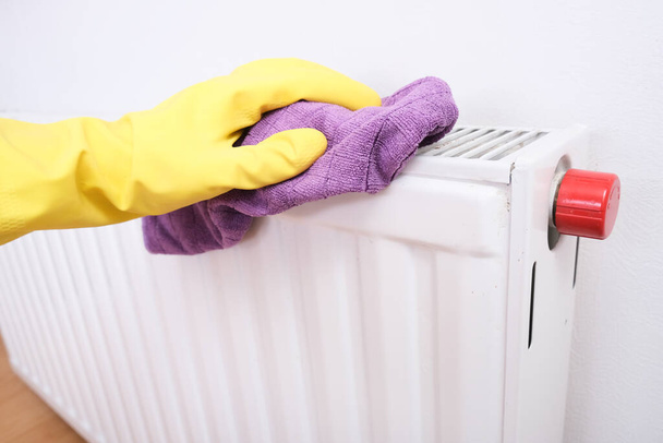 Radiator and house cleaning, hand in yellow rubber gloves wiping and washing central heating radiator with microfiber cloth - Fotografie, Obrázek