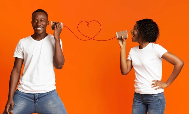 Young black couple with can phone on orange background - Foto, Bild