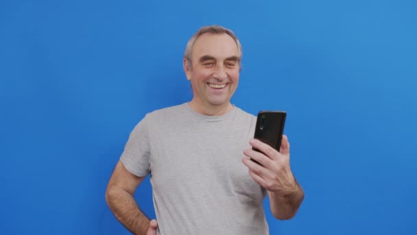 Happy senior elderly man holding smart phone watching mobile video calling online looking at screen. - Felvétel, videó