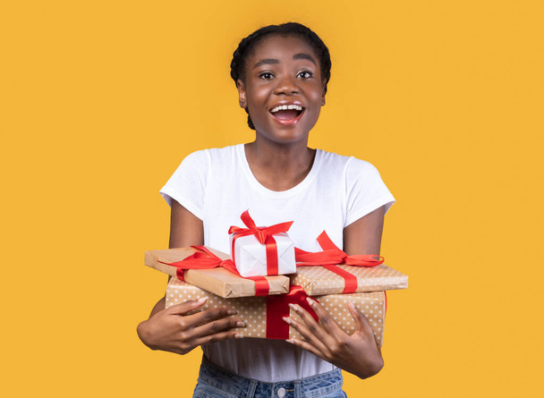 Emocionada mujer negra sosteniendo regalos envueltos posando sobre fondo amarillo - Foto, imagen