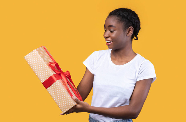 Glückliche afrikanische Dame hält Geschenkbox über gelbem Hintergrund - Foto, Bild