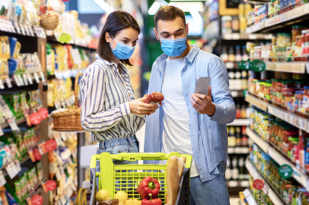 Mladá rodina v maskách s telefonem nakupování v supermarketu - Fotografie, Obrázek