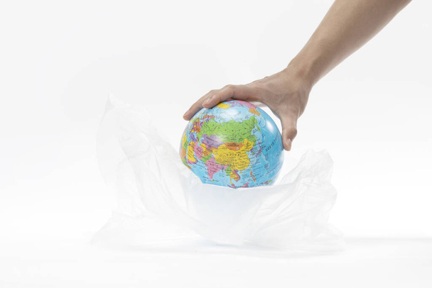 A closeup shot of a hand putting the globe in a plastic bag - environmental concept - Fotó, kép