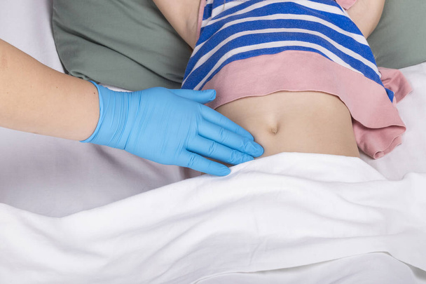 studio lighting. school age girl lies in bed doctor examines the belly. Close-up - Fotó, kép