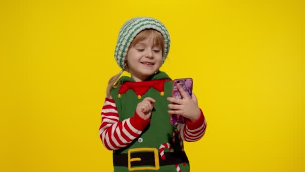 Niño niña en Navidad elfo Santa Claus ayudante traje haciendo una videollamada en el teléfono móvil - Imágenes, Vídeo