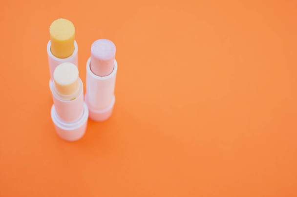 A closeup shot of hygienic lipsticks isolated on orange background - Foto, Imagem