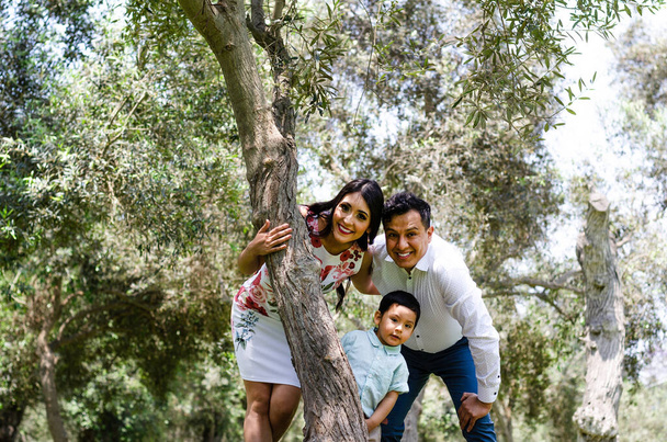 Ευτυχισμένη οικογένεια με άντρα, γυναίκα και παιδί να ακουμπάνε στο δέντρο στο πάρκο της πόλης. - Φωτογραφία, εικόνα