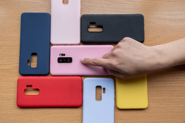 A top view of a hand pointing on a phone with colorful phone cases on a wooden table - Foto, immagini