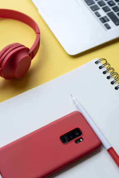 A vertical shot of a journal, marker pen, headphones, and a smartphone on a yellow background - Foto, Imagen