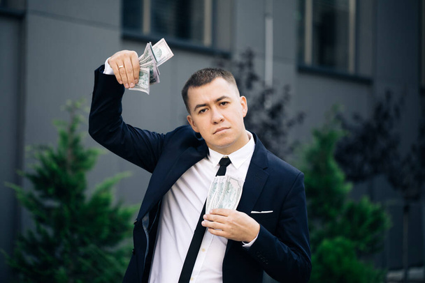 Man shows money and celebrating success, victory while looking to camera. Outdoors. Amazed happy excited businessman with money - U.S. currency dollars banknotes - 写真・画像