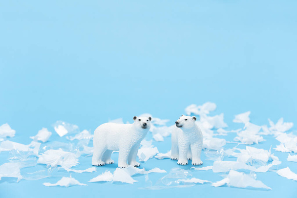 A closeup shot of polar bear toys surrounded with pieces of plastic and paper on a blue background - Фото, изображение