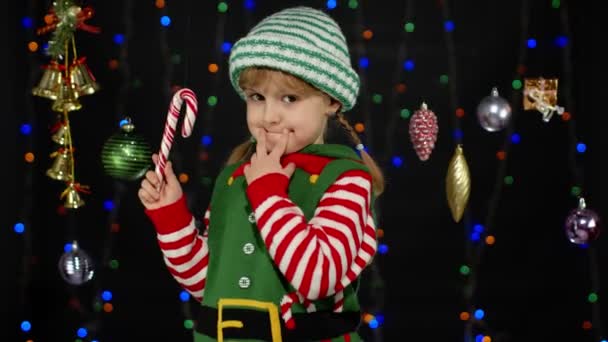 Dziecko dziewczyna w Boże Narodzenie elf Święty Mikołaj pomocnik kostium z cukierkiem trzciny lizak radosny uśmiech - Materiał filmowy, wideo