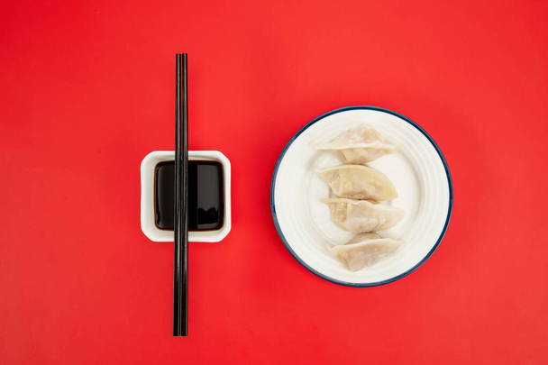 A top view closeup of cooked dumplings on a white plate next to a soy sauce on a red background - Фото, зображення