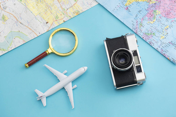A top view of a camera, airplane toy and magnifying glass on a blue background with a map - Foto, Imagem