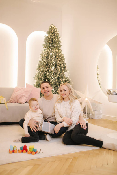 Mutlu bir anne, baba ve oğul ailesi Noel zamanı evde eğleniyor. Güzel dekore edilmiş odada şık bir aile. - Fotoğraf, Görsel