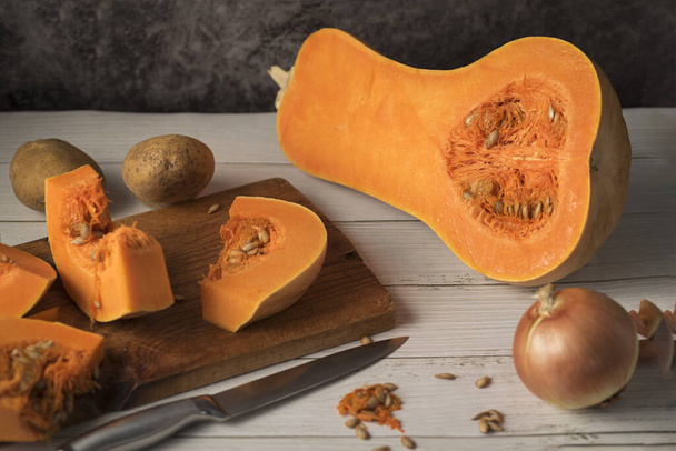 A selective focus shot of Butternut squash sliced on a cutting board with onion and potatoes - Photo, Image